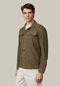 Camisa de manga larga color verde oliva en mezcla de algodón, con cuello, dos bolsillos delanteros, cierre de botones y dobladillo recto.