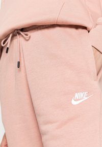 Ljusrosa Nike-joggers med mjukt tyg, justerbar dragsko med svarta spetsar och en vit logotyp på låret.