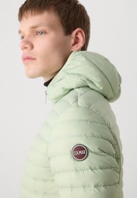 Svetlozelená prešívaná bunda s kapucňou na zips, s horizontálnym prešívaním a okrúhlym nášivkou loga Colmar na ľavom ramene.