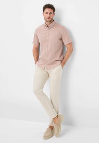 Camicia a maniche corte di un rosa chiaro con taschino sul petto, abbinata a pantaloni di lino color crema e scarpe slip-on beige.