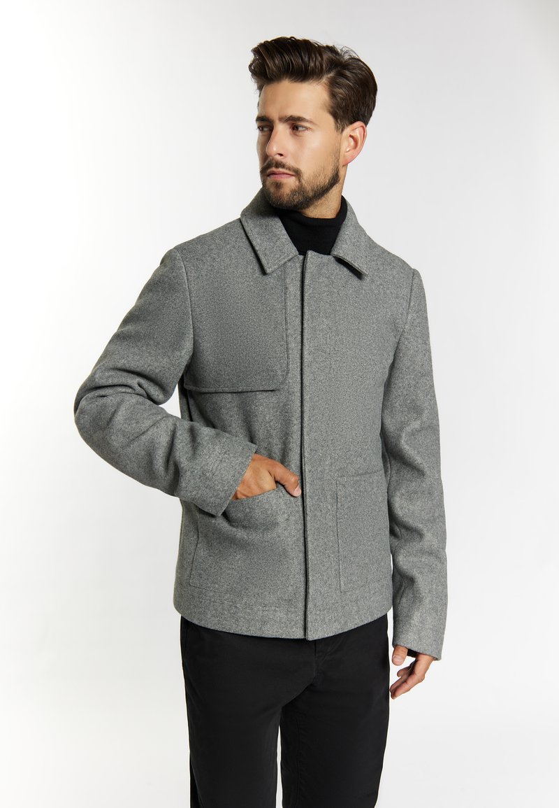 Grå uldblandingsjakke med klapkrave, to frontlommer, en ensartet tekstur og en lige pasform. Båret over en sort turtleneck.