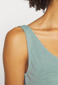 Ljusgrön linne med v-ringning, tillverkat av ett mjukt, texturerat tyg. Har tunna axelband och synliga detaljer på axlar och hals.