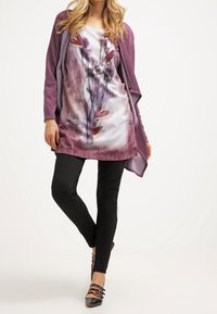 Cárdigan púrpura sobre una túnica con estampado floral en tonos blancos y burdeos. Leggings negros y zapatos negros con tiras completan el look.