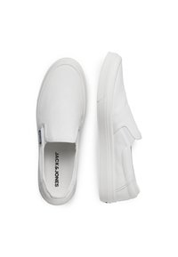 Fehér vászon slip-on cipők a JACK & JONES-tól, kerek orral, lapos gumi talppal és oldalsó címkével. Minimális dizájn, látható minták nélkül.