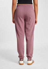 Hellrosa Jogginghosen mit elastischem Taillenbund, verjüngten Bündchen und glatter Textur, kombiniert mit weißen Sneakers mit braunen Details.