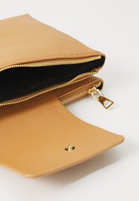 Clutch texturizado en tono marrón con cremallera y herrajes dorados. Diseño abierto que revela un interior negro. Forma plana con solapa redondeada y cierre magnético.