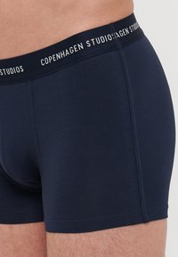 Sötétkék boxer alsók puha tapintással. Rugalmas anyag és egy derékpánt, amelyen fehér betűkkel szerepel a "Copenhagen Studios" felirat.