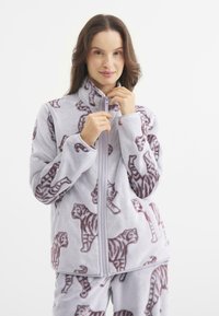 Kurtka polarowa w jasnoszarym odcieniu z powtarzającym się wzorem tygrysa w ciemnobrązowym kolorze. Posiada wysoki kołnierz i zamek błyskawiczny na pełnej długości.