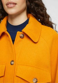 Orange wool blend jacket featuring a collared neckline, front button closure, and two spacious pockets with rounded wooden buttons.