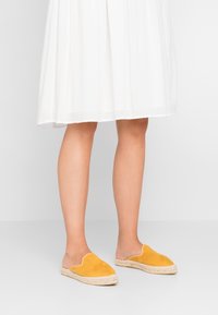 Gula mockaskor med slip-on-design och vävda jutesulor, med en scallop-mönster längs den övre kanten.