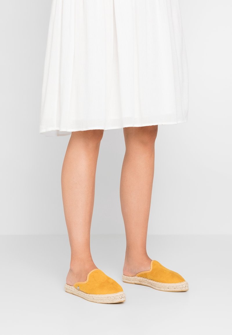 Gula mockaskor med slip-on-design och vävda jutesulor, med en scallop-mönster längs den övre kanten.