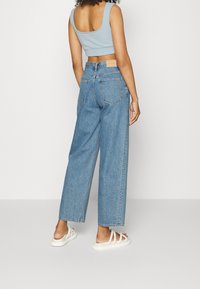 Jasnoniebieski crop top w połączeniu z luźnymi, wysokimi dżinsami w kolorze niebieskim. Dżinsy mają tylne kieszenie i prosty krój nogawek. Białe sandały.