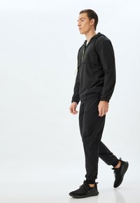 Svart lättvikts träningsoverall med zippered huva, elastiska ärmslut och slim-fit byxor. Har gröna detaljer och texturerad tyg.