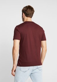 Bordeaux T-shirt met korte mouwen en ronde hals, gemaakt van soepel katoen. Achteraanzicht toont een getailleerd ontwerp en schone naden.