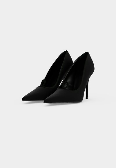 Paire de chaussures à talons hauts noires à bout pointu avec talons fins sur un fond clair uni.