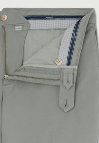 Lichtgrijze pantalons met gedeeltelijk open ritssluiting van messing, twee beige knopen en een merkband aan de binnenkant van de tailleband met de tekst "Hackett."