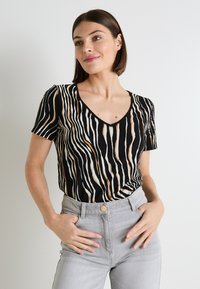 Camiseta de rayas blanco y negro con escote en V. Hecha de tela ligera, presenta variaciones horizontales y verticales en el ancho de las rayas.