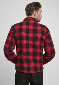 Camisa de franela a cuadros roja y negra, con mangas largas, un cuello con solapa y un dobladillo curvado, hecha de una suave tela texturizada.