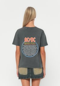 Szara bawełniana koszulka z grafiką z tyłu, zawierającą napis "AC/DC", okrągły wzór oraz listę miejsc koncertów w niebieskich i pomarańczowych kolorach.