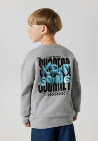 Sudadera gris con cuello redondo que presenta texto impreso en negro y letras azules en relieve que dicen "KEEP GOING" en la parte posterior.