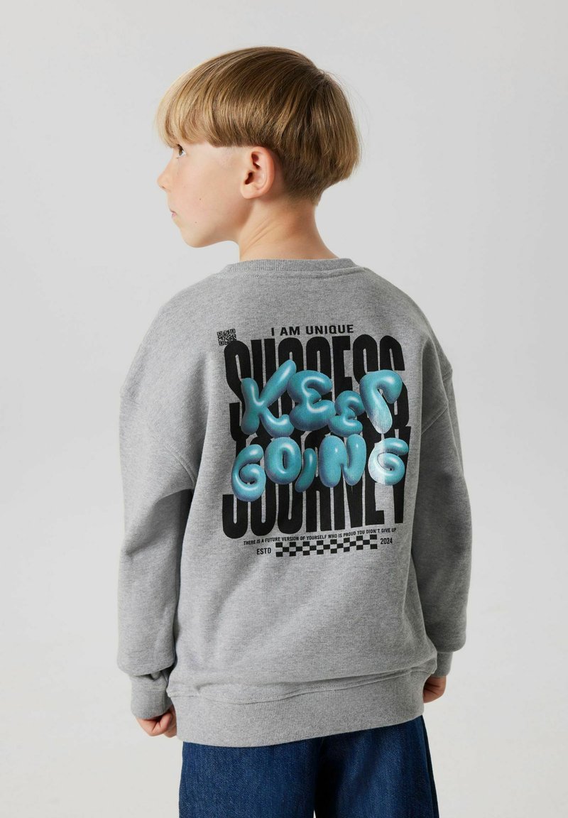 Sudadera gris con cuello redondo que presenta texto impreso en negro y letras azules en relieve que dicen "KEEP GOING" en la parte posterior.