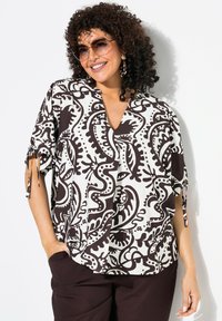 Haut léger à motifs noir et blanc avec un décolleté en V, des manches courtes et des liens sur les côtés. Associé à un pantalon marron foncé.