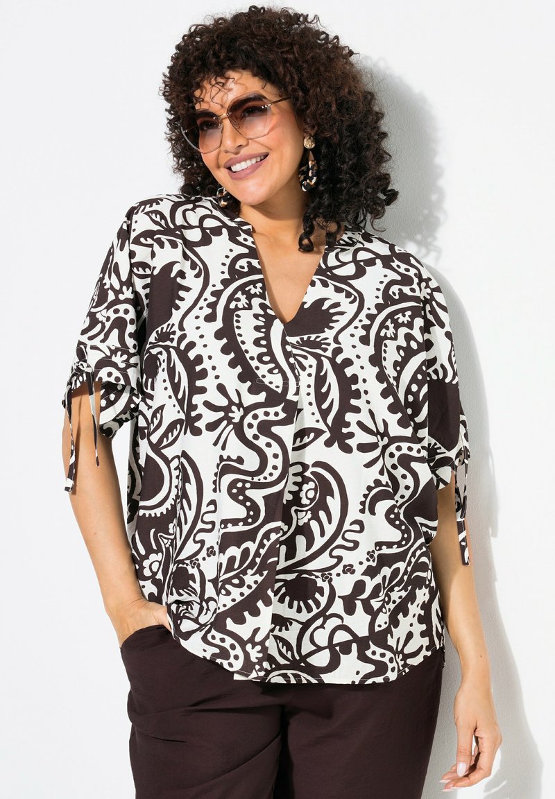 Haut léger à motifs noir et blanc avec un décolleté en V, des manches courtes et des liens sur les côtés. Associé à un pantalon marron foncé.