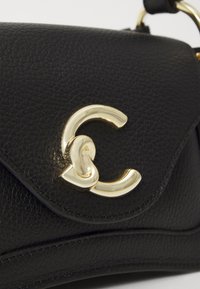 Sac en cuir noir avec une surface texturée, des éléments en or courbés et un accent de logo entrelacé distinctif sur le rabat.