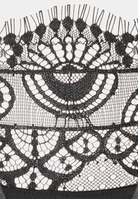 Tecido de renda preta com padrões intrincados de curvas e pontos, com uma textura delicada e bordas em forma de concha ao longo da parte superior.