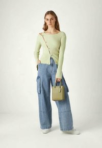 Light green ribbed knit top with asymmetrical neckline and button detail, paired with wide-leg light blue cargo jeans and small green handbag.