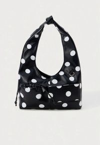 Czarna torebka z czarnej skóry ekologicznej z dużymi białymi kropkami, pojedynczym uchwytem, kieszenią ze ściągaczem oraz płaską przednią kieszenią. Miękka faktura, kształt hobo.