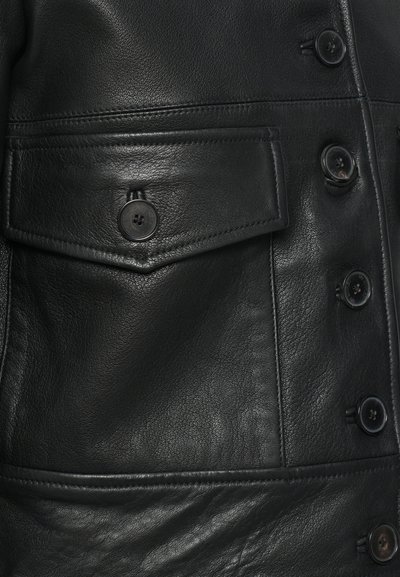 Zwarte leren jas met een gladde textuur, voorzien van een borstzak, donkere knopen en op maat gemaakte stiksels langs de randen.