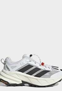 Λευκό και μαύρο παπούτσι για ορεινό τρέξιμο Adidas Terrex με παχιά σόλα, μαύρες ρίγες και ετικέτα Gore-Tex στο πλάι.