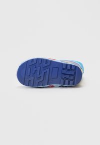 Suela de sneaker de goma azul con un patrón de agarre texturizado, que presenta puntos coloridos en rojo, amarillo y azul cerca de la punta. Diseño plano.