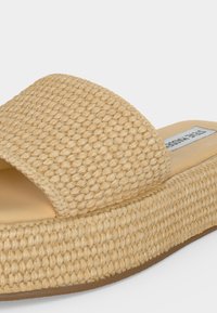Sandale beige tissée à plateforme avec une large bride et une semelle rembourrée, avec un bout carré et une étiquette à l'intérieur.