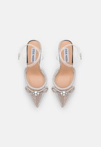 Paire d'escarpins argentés à bout pointu avec des brides de cheville transparentes, ornés de strass et de nœuds décoratifs sur les bouts.