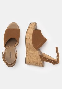 Braune Wildleder-Wedgesandalen mit einem Kork-Absatz. Sie verfügen über eine offene Zehenpartie, einen Knöchelriemen mit Schnalle und eine weiche, strukturierte Oberfläche.