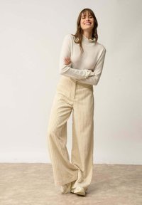 Beige, gerippte weit geschnittene Hose kombiniert mit einem hellen Creme, enganliegenden Rollkragenpullover. Der Stoff wirkt weich mit einer strukturierten Oberfläche.