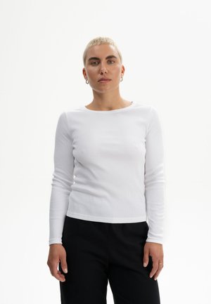 Langärmliges, weißes, geripptes Shirt mit rundem Ausschnitt. Stricktextur und taillierte Passform. Kombiniert mit schwarzen Hosen. Schlichte und klare Ästhetik.