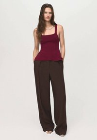 Burgundy neulottu hihaton paita leveillä hihnoilla ja peplum-helma yhdistettynä korkeavyötäröisiin, löysiin ruskeisiin housuihin ja avokärkisiin jalkineisiin.