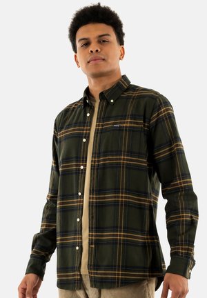 Groene en gele geruite button-up shirt met een borstzak en witte knopen, gelaagd over een beige shirt. Het heeft lange mouwen en een kraag.