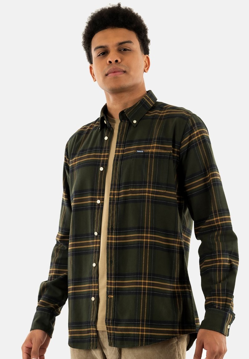 Groene en gele geruite button-up shirt met een borstzak en witte knopen, gelaagd over een beige shirt. Het heeft lange mouwen en een kraag.