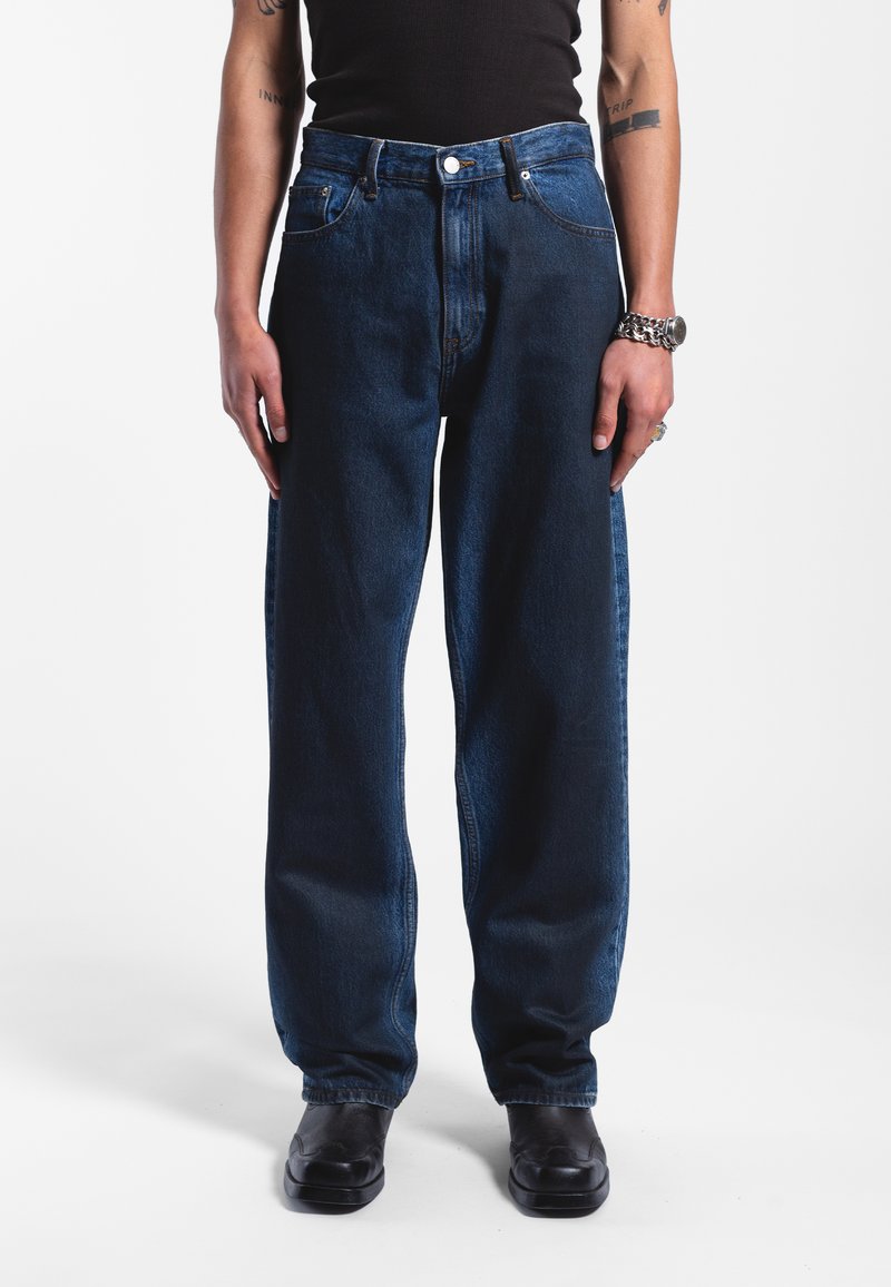 Tmavě modré džíny s rovnými nohavicemi, pěti kapsami a vysokým pasem. Nosit s černými botami, které mají hladký povrch.