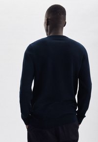 Granatowy sweter wełniany z okrągłym dekoltem, ribbowanymi mankietami i dołem, z teksturowanym wzorem. Widok z tyłu.
