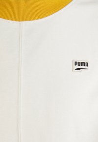 Sudadera blanca con un cuello acanalado amarillo y un logotipo de Puma bordado en negro en el pecho. Textura suave, diseño casual.