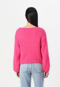 Pink knitted sweater with a loose fit, wide sleeves, and a ribbed hem, paired with light blue jeans. Texture appears soft and fluffy.