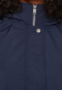 Mörkblå jacka med dragkedja fram, tryckknappsstängning och rynkat tyg runt kragen; slät textur med minimal detaljering.