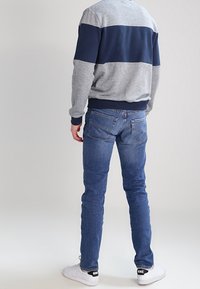 Grå och marinblå färgblockerad sweatshirt med ribbade ärmslut, tillsammans med åtsittande blå denimjeans. Skorna är vita med svarta accenter.