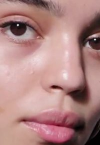 Nærbillede af et ansigt med glat, lys hud. Brune øjne, markeret næse og fyldige læber. Ingen synlig make-up, naturlig struktur og farve.