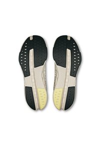 Semelles de chaussures avec une surface en caoutchouc noir texturé, une semelle intermédiaire crème avec un motif alvéolaire, et des zones d'accent jaune vif.
